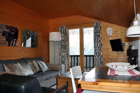 A cozy cabin interior with a wooden interior, a sofa, a dining table, and a mounted TV.
