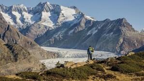 Una persona de pie sobre un saliente rocoso, con un glaciar y montañas al fondo.