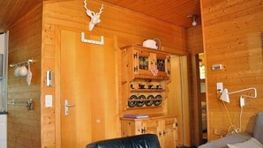 Interior de una cabaña de madera con una mesa de comedor, una silla de cuero negro y un mueble con vajilla.