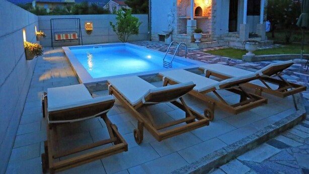 A swimming pool with lounge chairs and a stone-tiled deck. - Apartment Ana With Private Pool (Solin)