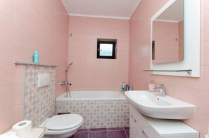 A bathroom with a bathtub, toilet, sink, and a small window.