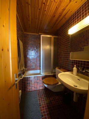 A compact bathroom with a wooden ceiling, a toilet, a sink, and a window with a view.
