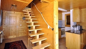 A wooden interior with a staircase leading to a second floor, a kitchen with wooden cabinets, and a small island counter. - Harpa OG (Bettmeralp)