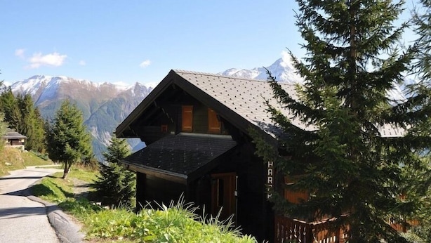 A wooden cabin with a sloped roof, surrounded by trees and mountains. - Harpa OG (Bettmeralp)