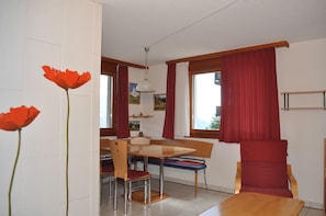 Un comedor con una mesa y sillas de madera, cortinas rojas y un cuadro en la pared.