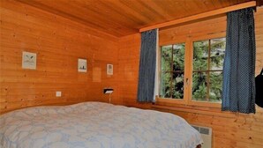 A wooden cabin room with a bed, a window with curtains, and framed pictures on the wall. - Jadwiga OG (Bettmeralp)