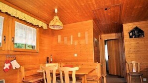 A wooden interior with a dining table and chairs, a hanging light fixture, and a small window with a view. - Jadwiga OG (Bettmeralp)