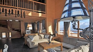 Ein großzügiger Wohnbereich mit hoher Decke, einer Holztreppe und einem großen Fenster mit Blick auf die Berge.