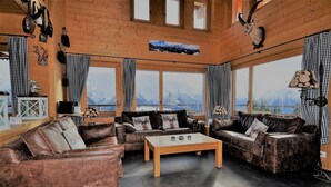 Ein gemütliches Wohnzimmer mit Ledersofas, einem Holztisch und großen Fenstern mit Blick auf die Berge.