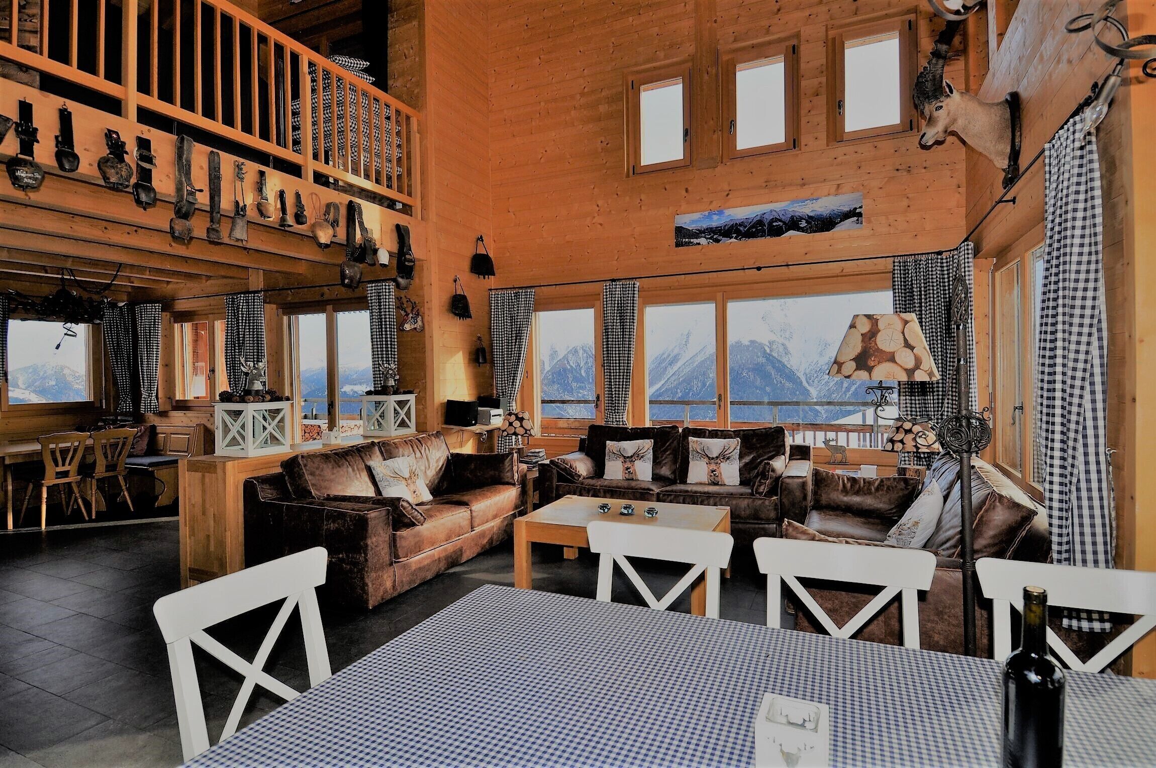 A cozy lodge with wooden interiors, a loft area with a wooden railing, and a view of mountains through large windows.