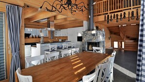 Ein Holzinterieur mit einem Esstisch, weißen Stühlen, einem Steinkamin und einer hängenden Leuchte.