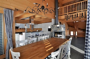 A wooden interior with a dining table, white chairs, a stone fireplace, and a hanging light fixture. - Laackerhof (Bettmeralp)