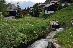 Un pueblo montañoso con casas tradicionales, un pequeño arroyo y un puente.