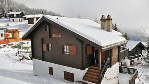 Un chalet de madera con techo inclinado, una escalera que lleva a la entrada y un paisaje cubierto de nieve.