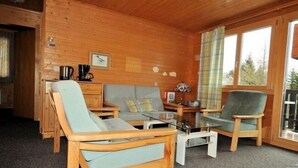 Una habitación acogedora con paredes de madera, un sofá, dos sillones, una mesa de centro y una mesita con una tetera y tazas.