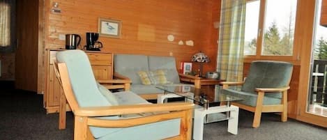 A cozy room with wooden walls, a sofa, two armchairs, a coffee table, and a small table with a kettle and cups.