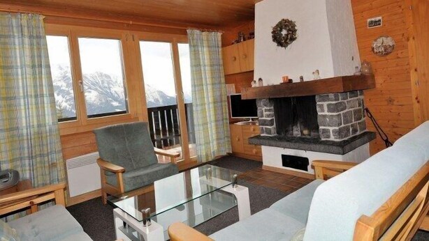 Una sala de estar acogedora con chimenea de piedra, paredes de madera y amplios ventanales con cortinas.