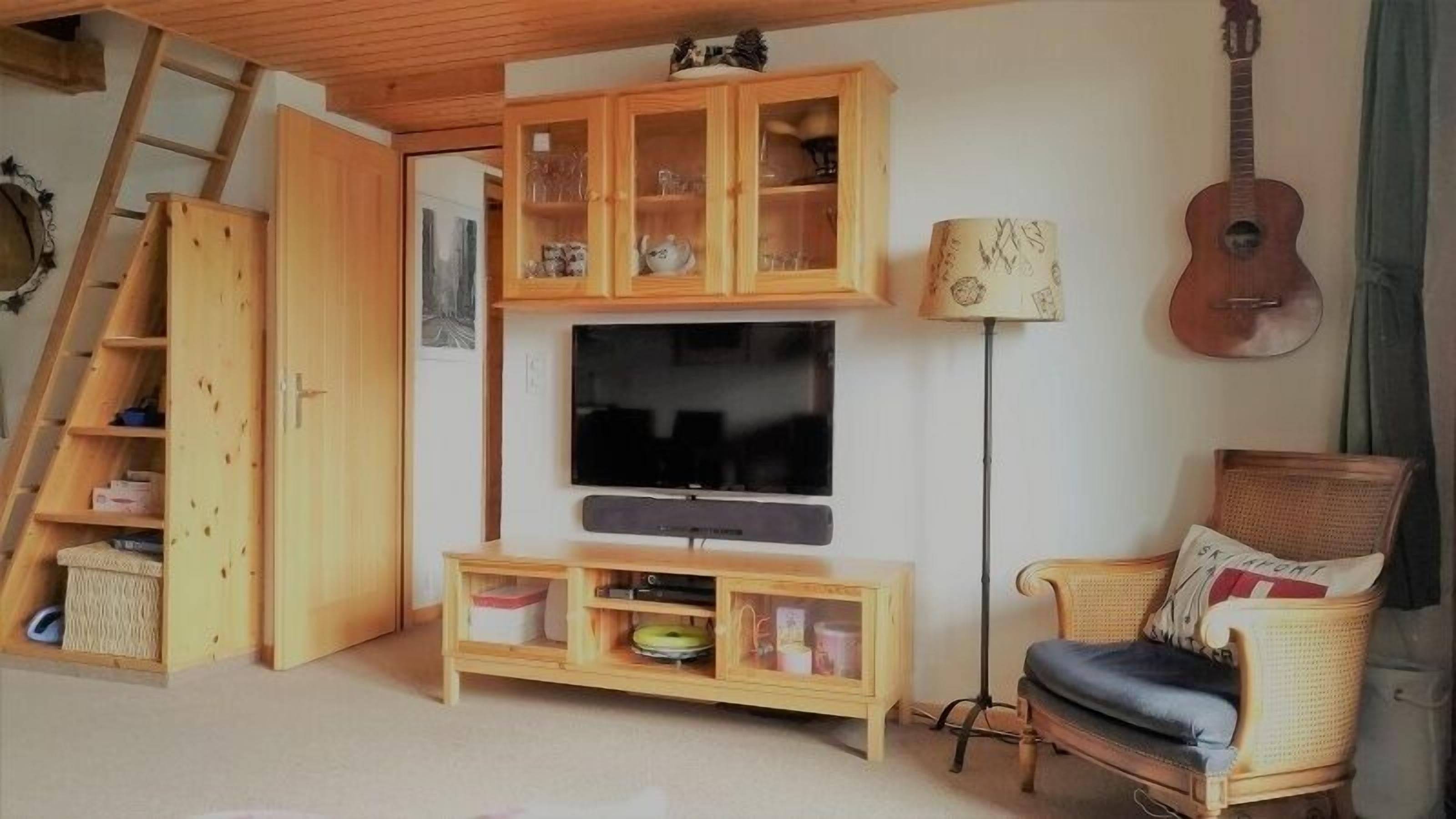 Ett mysigt vardagsrum med en tv, träskåp, en gitarr, en stol och en stege.