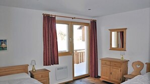 A bedroom with two beds, a wooden wardrobe, a mirror, and a sliding glass door leading to a balcony. - Mon Reve Bergh (Bettmeralp)