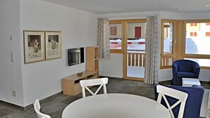 A living room with a round table, white chairs, a blue armchair, a television, and framed pictures on the wall. - Mon Reve Bergh (Bettmeralp)