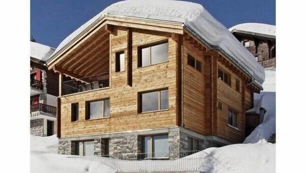 Eine Holzhütte mit Steinunterbau, mehreren Fenstern und einem Balkon, umgeben von Schnee.