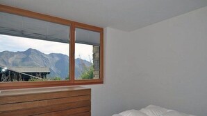 Ein Schlafzimmer mit einem hölzernen Kopfende, einem Bett mit weißer Bettwäsche und einem Fenster mit Blick auf die Berge.