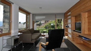 Ein modernes Wohnzimmer mit einer Couch, einem schwarzen Sessel, einem Fernseher und einem Holzregal.