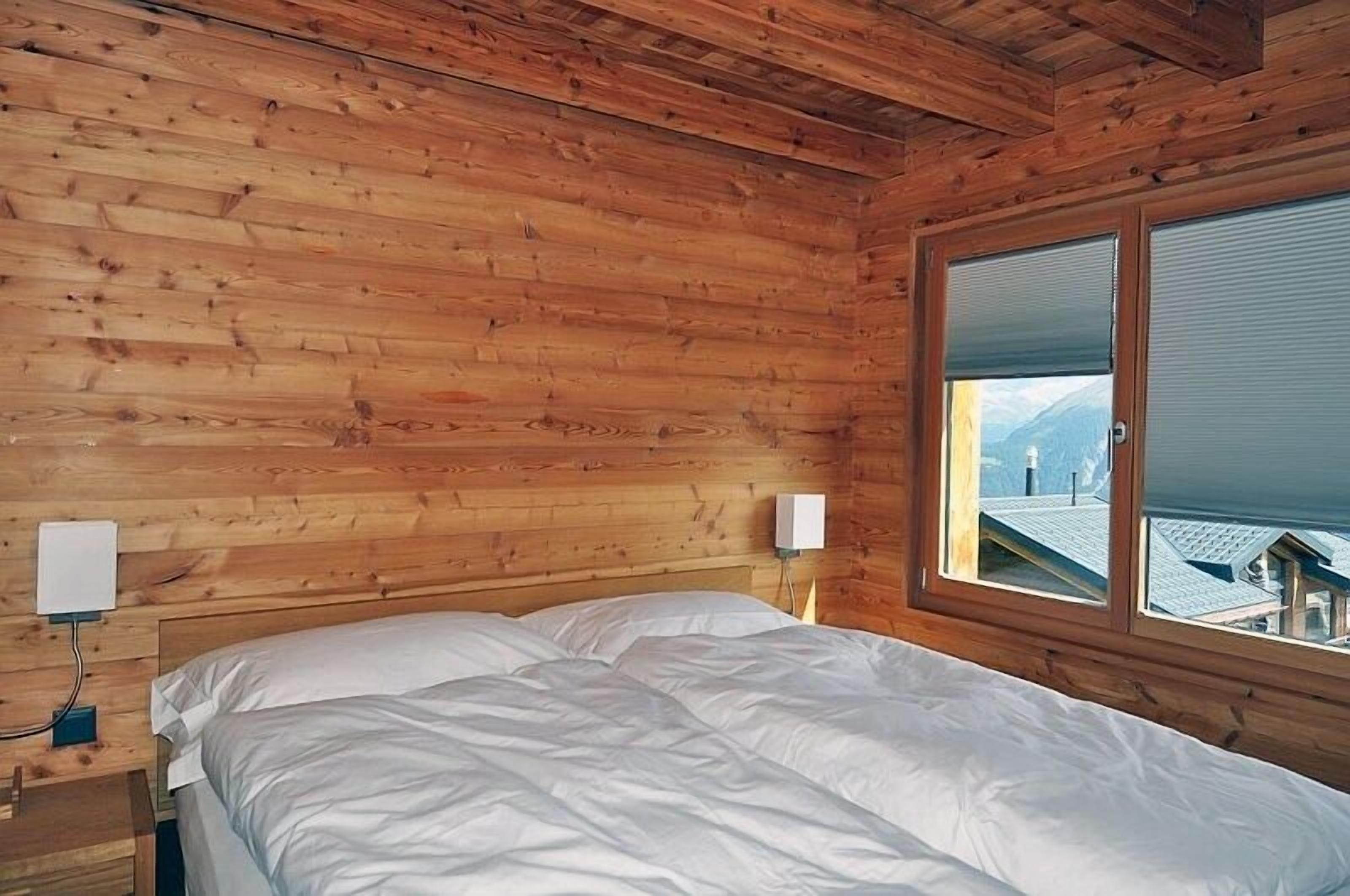 A wooden cabin room with a bed, two bedside tables, and a window with a view of a mountain.