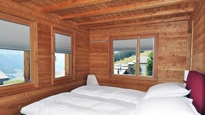 A wooden cabin room with a bed, large windows, and a view of a mountain landscape. - Nachtigall OG (Bettmeralp)