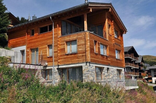 A multi-story wooden cabin with stone foundation, balconies, and large windows.