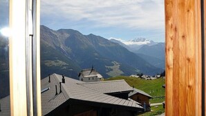 A mountain view from a window with a wooden frame, overlooking a valley with houses and mountains. - Nachtigall OG (Bettmeralp)