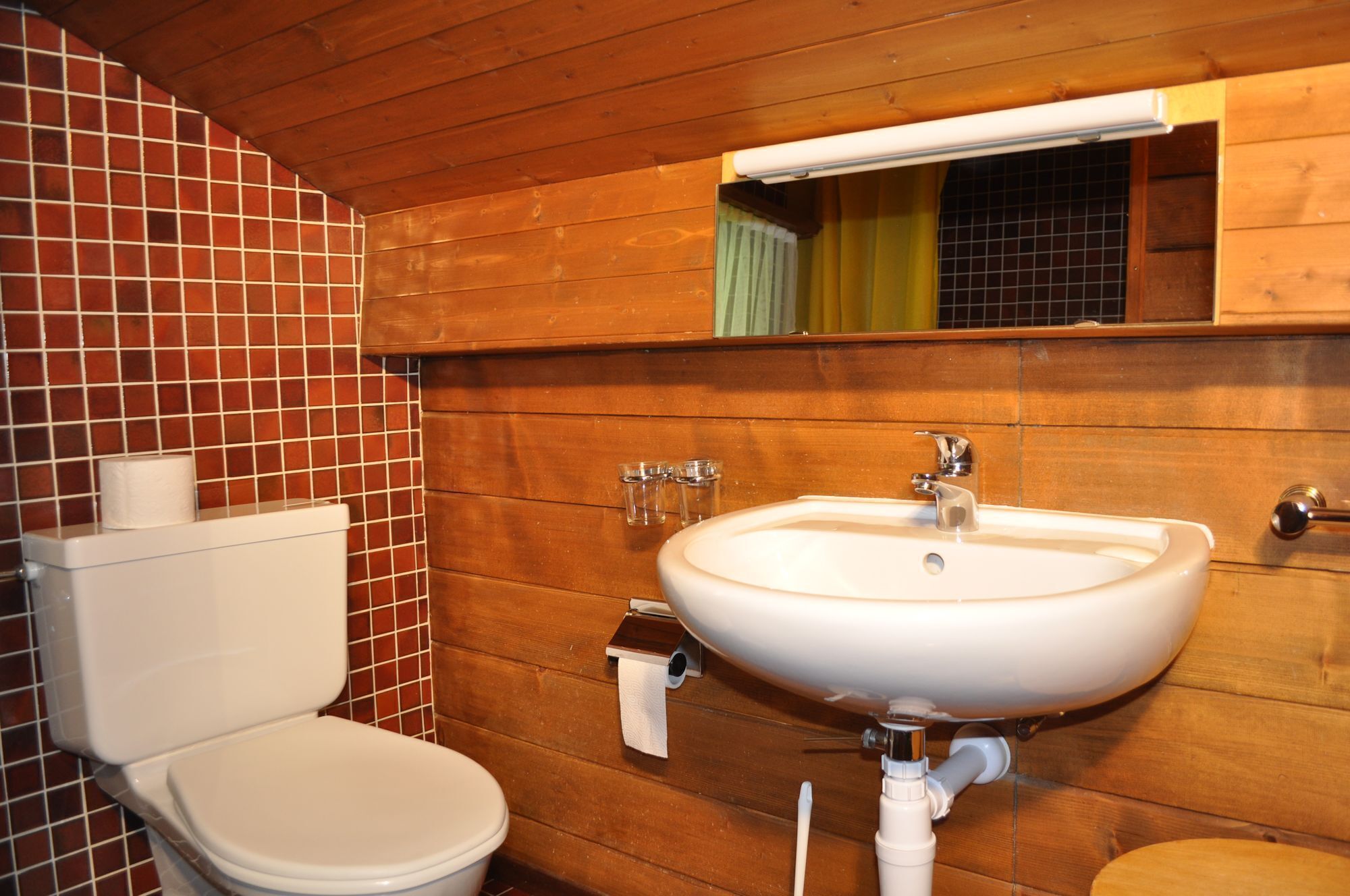 A bathroom with a toilet, sink, and wooden walls.