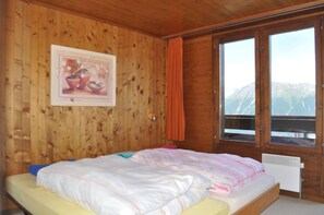 Une chambre à coucher dans une cabane en bois, avec un lit, un tableau encadré au mur et une fenêtre donnant sur les montagnes.