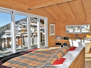 A wooden cabin with a large bed, a bathroom, and a view of a snowy village. - Rupicapra (Bettmeralp)