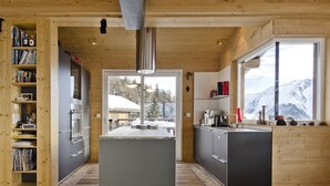 A modern kitchen with a central island, wooden cabinetry, and a view of snowy mountains through large windows. - Rupicapra (Bettmeralp)