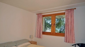 Une chambre avec deux lits, une fenêtre avec des rideaux, une table de chevet avec une lampe et une chaise.