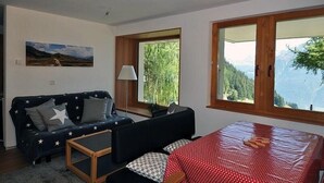 Une pièce comprenant un canapé, une petite table, un lit, un tableau accroché au mur et de grandes fenêtres offrant une vue sur les montagnes.