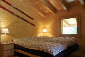 A wooden cabin bedroom with a bed, two bedside lamps, a window, and skis leaning against the wall. - Sternschnuppe OG (Bettmeralp)