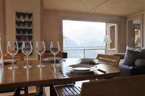 Una zona de menjador amb taula de fusta preparada per a quatre persones, vista a les muntanyes a través d'un gran finestral i un disseny interior modern.