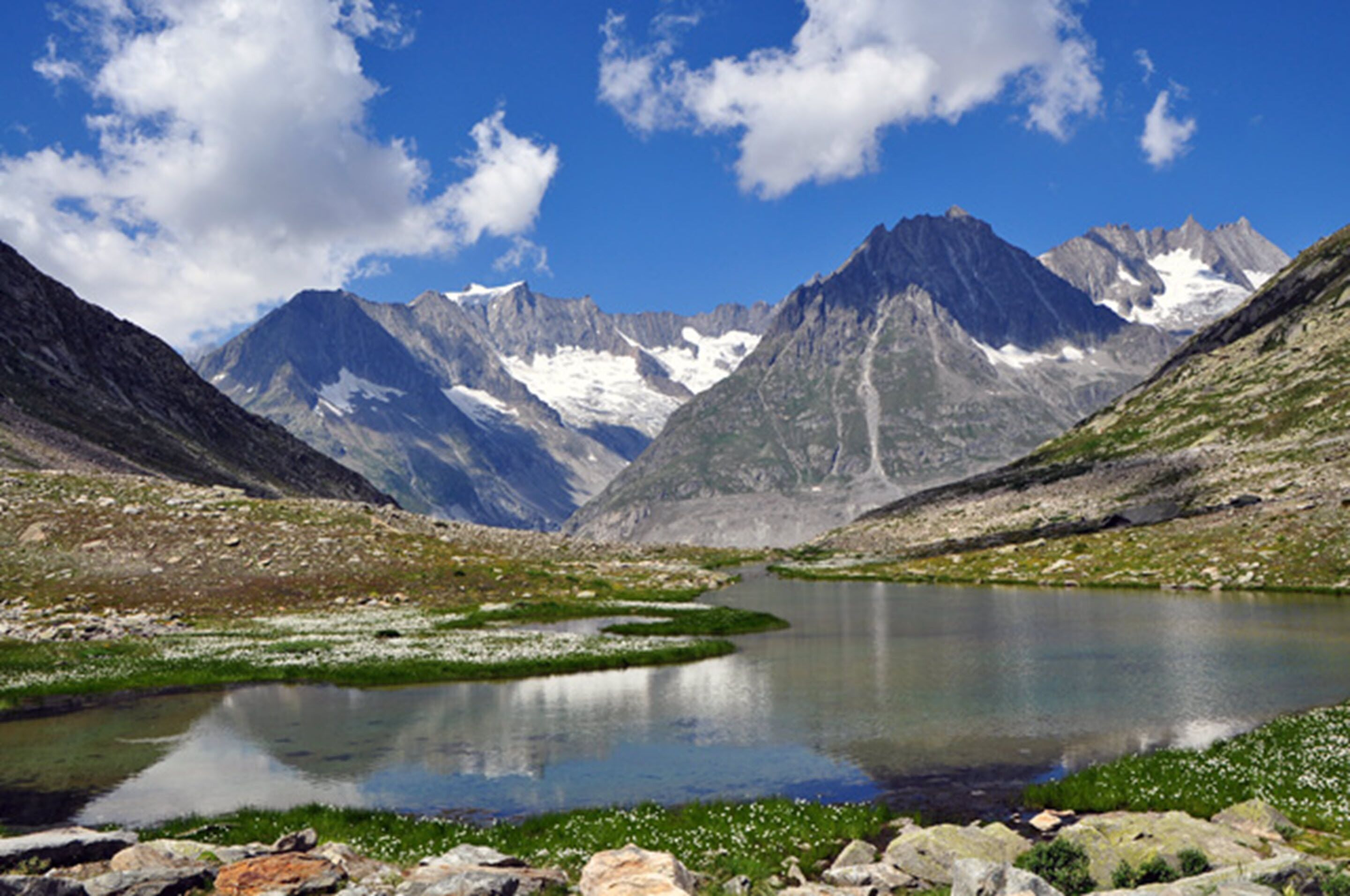 Eine Berglandschaft mit einem See, felsigem Gelände und schneebedeckten Gipfeln.