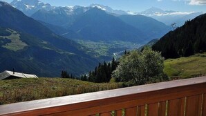 Un paisaje montañoso con un valle, una valla de madera y picos nevados en la distancia.