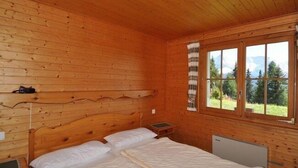 Habitación de cabaña de madera con dos camas, una ventana que ofrece vistas a árboles y montañas, y un cabecero de madera.