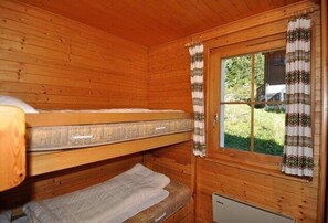 A wooden cabin room with bunk beds, a window with curtains, and a small radiator. - Toggi EG (Bettmeralp)