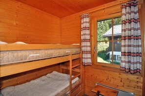 A cabin with wooden walls, a bunk bed, a window with curtains, and a small table.