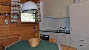 A compact kitchen with wooden walls, a large hanging light fixture, a window with curtains, and a sink. - Toggi OG (Bettmeralp)