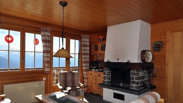 A cozy cabin with a stone fireplace, wooden furniture, and large windows offering mountain views. - Toggi OG (Bettmeralp)