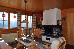 A cozy cabin with a stone fireplace, wooden furniture, and large windows offering mountain views. - Toggi OG (Bettmeralp)