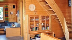 Un intérieur en bois avec un espace nuit en mezzanine, une bibliothèque intégrée et une fenêtre agrémentée d’un rideau coloré.
