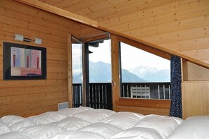 A wooden cabin room with a bed, a window with a mountain view, and a framed picture on the wall.