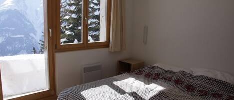 A bedroom with a bed, a window with a view of mountains, and a radiator.